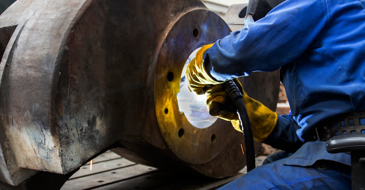 A welder wearing safety gear operates on a large metal component in an industrial setting.